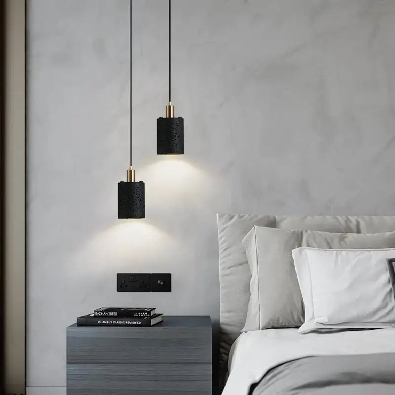 Decorbites black hole stone chandelier with black cylindrical textured pendant lights and gold-tone accents above bedside table