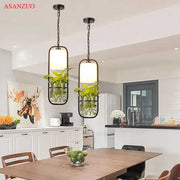 Decorbites black iron cage pendant light in black metal with rectangular frames and integrated plant holders emitting warm glow