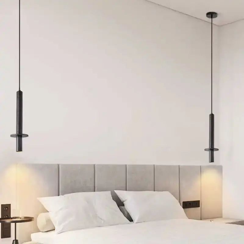 Two sleek decorbites black iron led pendant lights in black iron hang symmetrically above a bed with tufted gray headboard