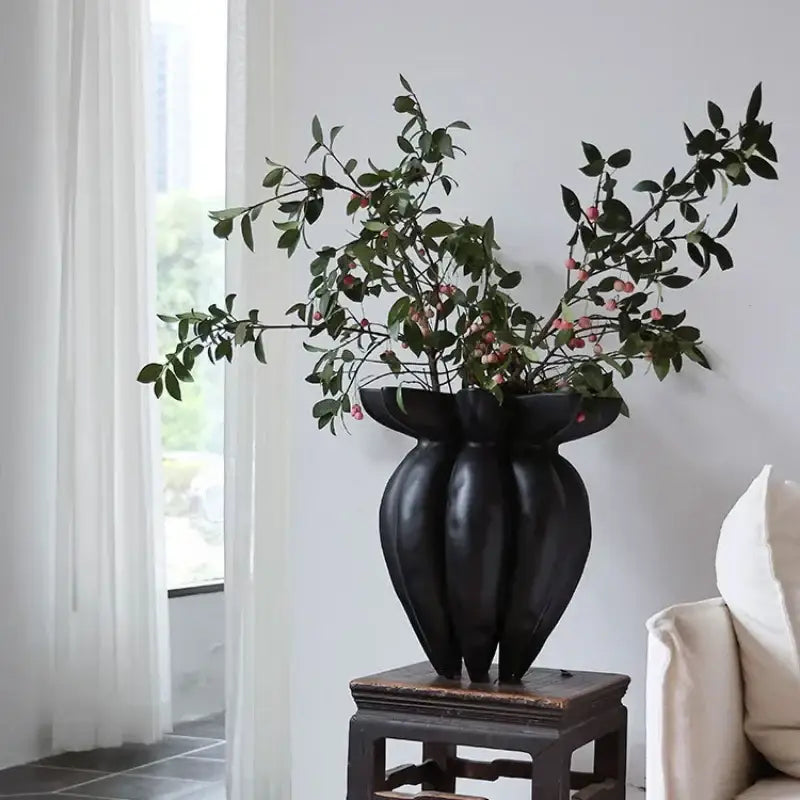 Black jellyfish petal black ceramic vase with sculpted ridges and wide opening holding greenery with pink berries