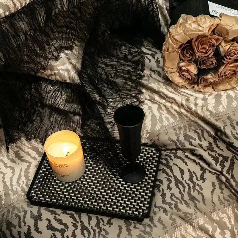 A black lacquered champagne flute rests on a woven tray beside a candle with decorbites black lace leopard print 1000tc bedding set