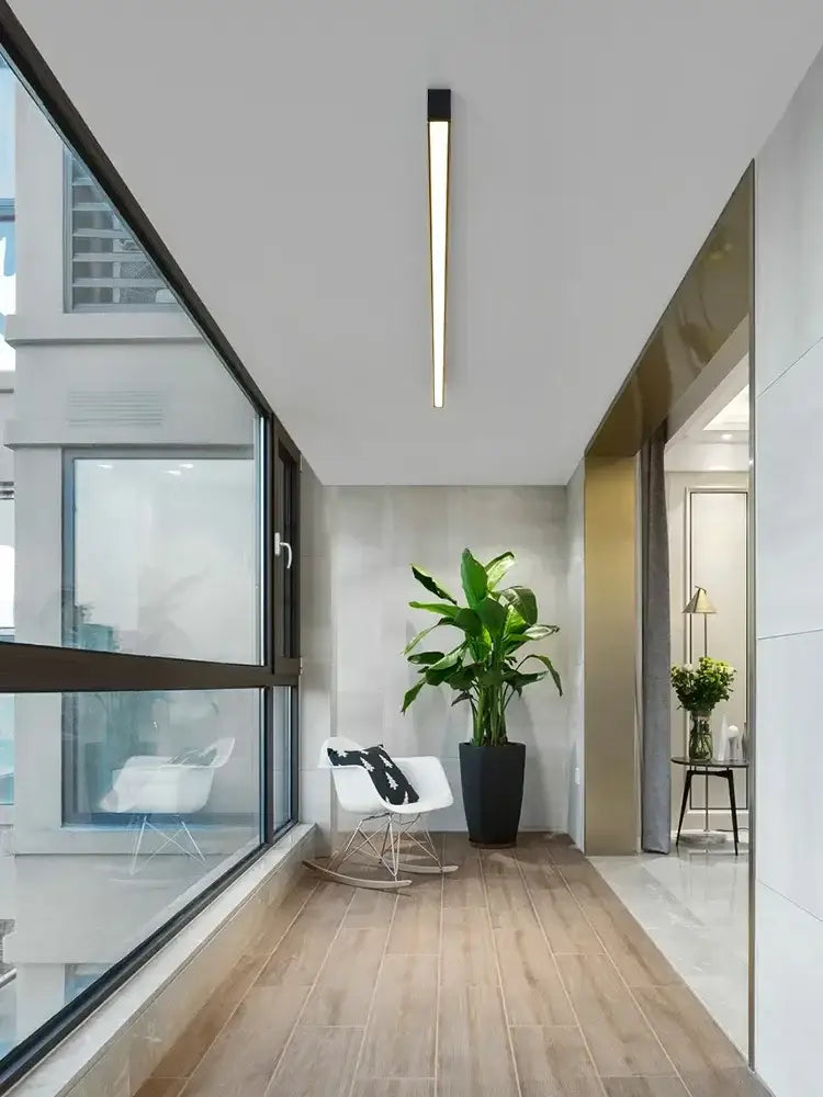 A sleek modern minimalist hallway illuminated by the decorbites black linear led ceiling lamp with a tall potted plant center