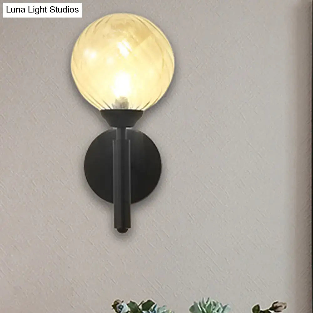 Modern black wall sconce with warm-toned spherical clear textured glass globe for bedroom lighting