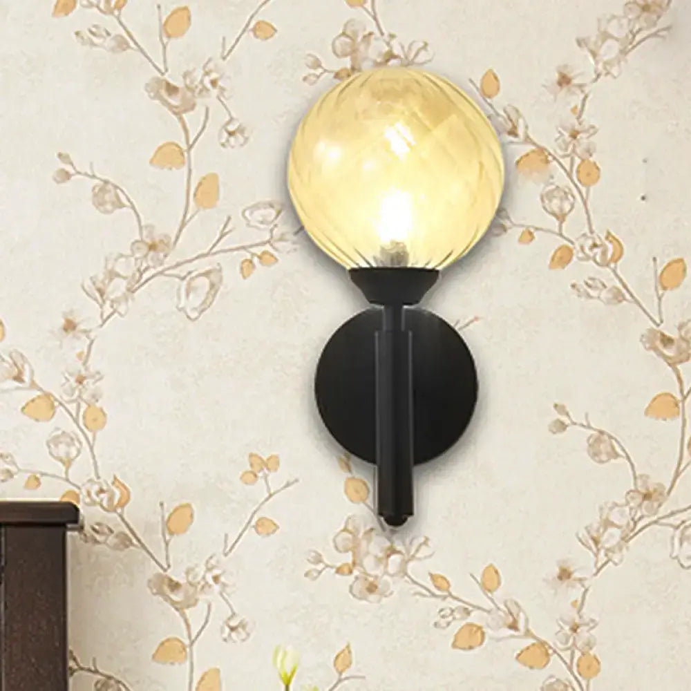 Modern black wall sconce with clear textured glass featuring a warm amber spherical globe for bedroom lighting