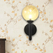 Modern black wall sconce with clear textured glass featuring a warm amber spherical globe for bedroom lighting