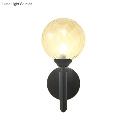 Modern black wall sconce with clear textured glass amber-toned spherical globe and black metal base for bedroom lighting