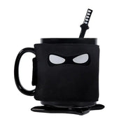 A decorbites black ninja mug with matte finish and white eye cutouts featuring a matching black sword stirrer