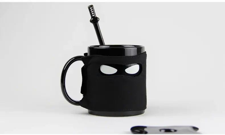 Decorbites black ninja mug with sword stirrer featuring glossy black finish and eye-shaped cutouts for kitchen novelty use