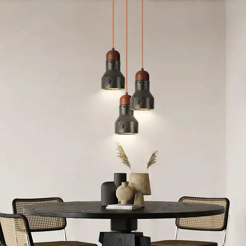 Three decorbites black travertine led pendant lamps with matte black metal and reddish-brown ceramic tops hang on orange cords