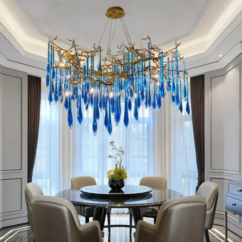 Decorbites blue crystal chandelier with striking blue glass and gold branching arms hanging above dining table
