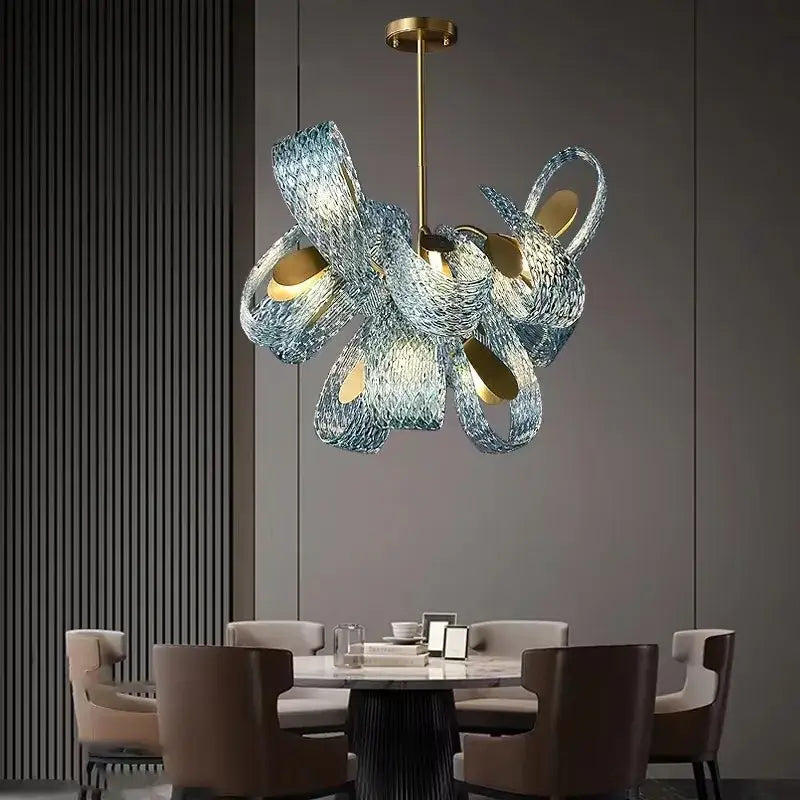 Modern sculptural pendant lamps with intertwined blue glass led ribbons and gold-toned circular light fixtures by DecorBites