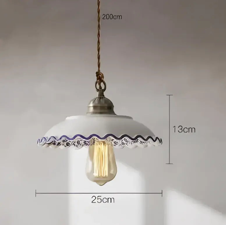 A vintage-style pendant light with white ceramic shade and purple lace trim suspended by braided cord with Edison bulb