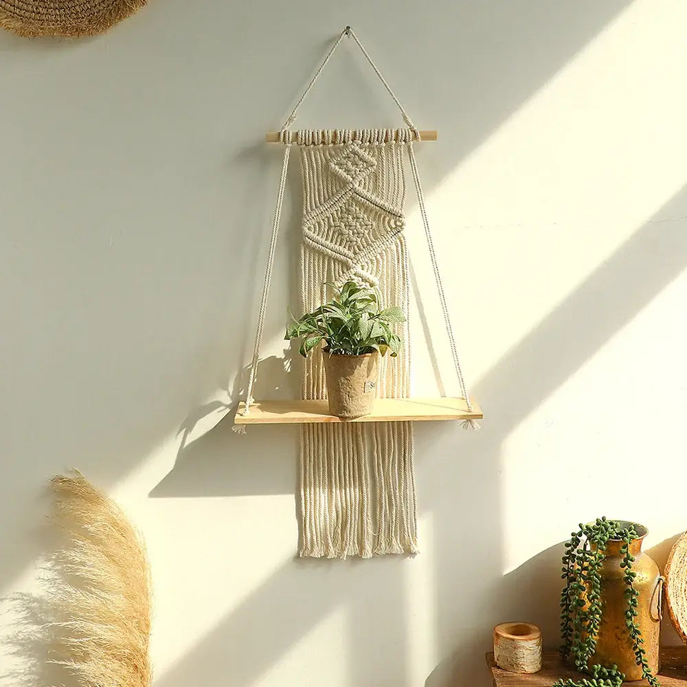 Beige macrame hanging shelf with wooden wall shelf holding potted plant for boho home decor by decorbites