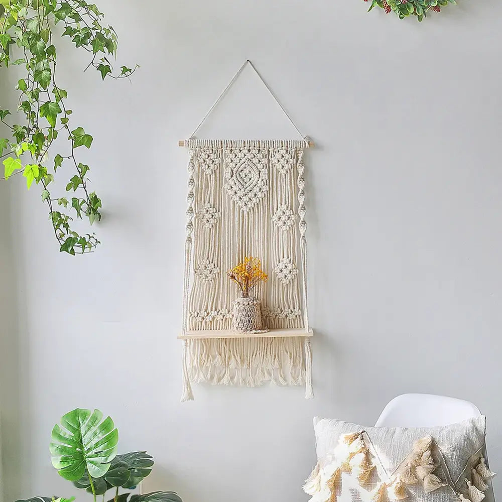 Cream-colored macrame hanging shelf with wooden shelf and tassels for boho wall shelf home decor by DecorBites™