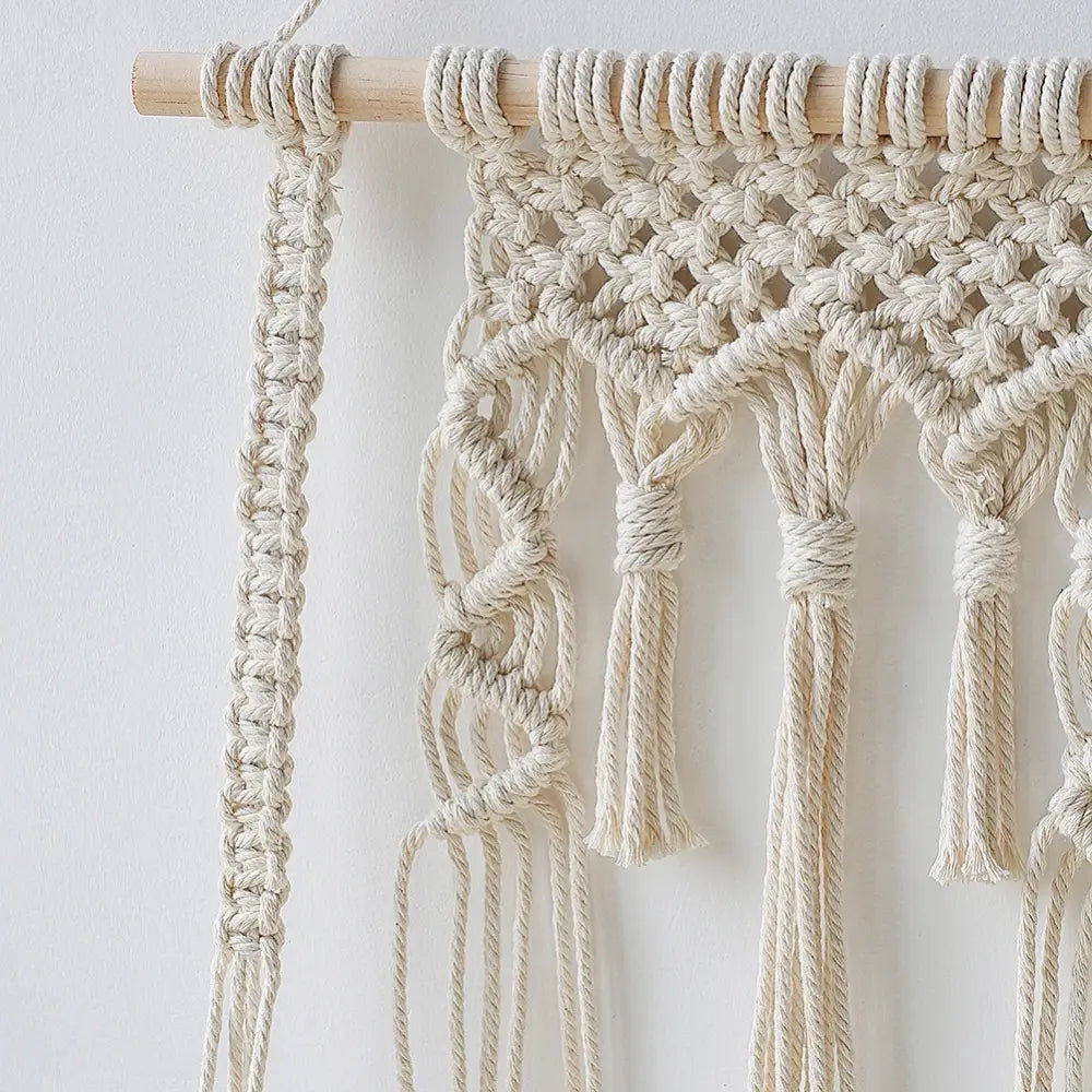 Cream-colored macrame wall shelf with intricate knotting and tassels made from natural fiber rope for home decor