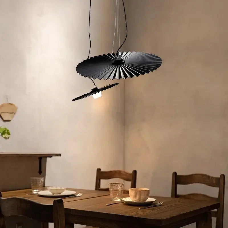 Black pleated fan-shaped pendant light with wood details hanging above dining table from decorbites boomerang wood chandelier collection