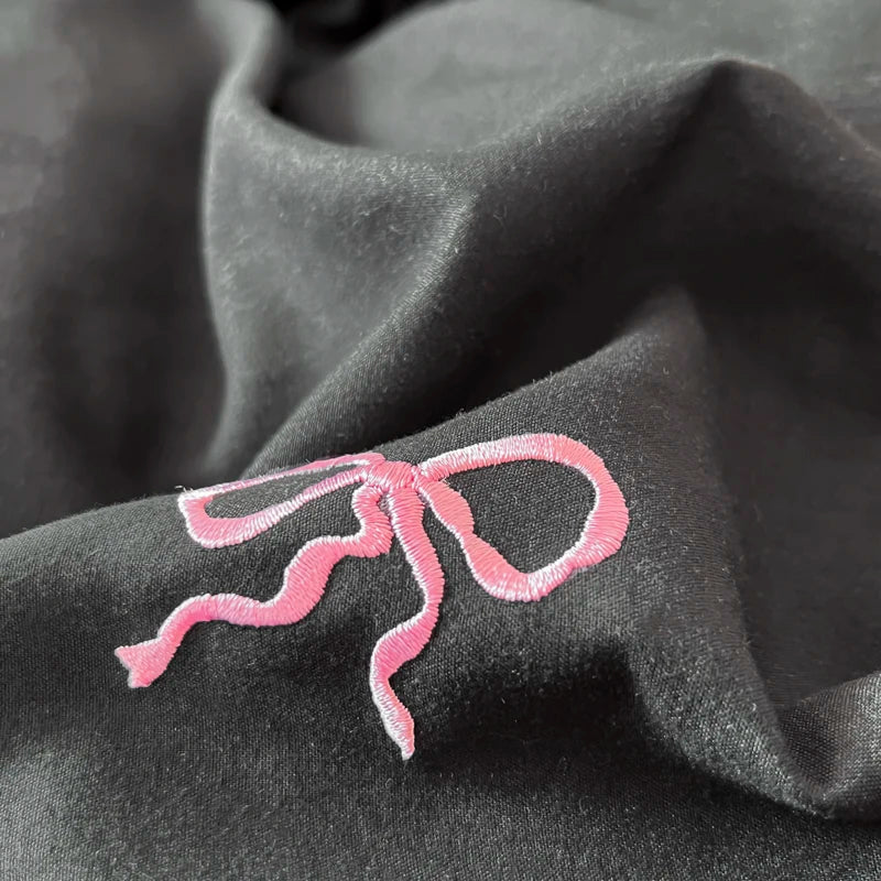 A delicate pink bow embroidery adorns dark fabric in the DecorBites™ bow embroidery bedding set with ruffles
