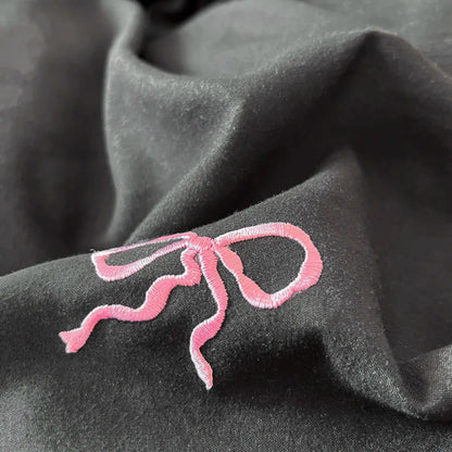 A delicate pink bow embroidery adorns dark fabric in the DecorBites™ bow embroidery bedding set with ruffles