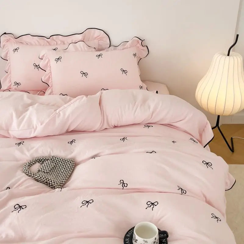 Pink satin DecorBites™ bow embroidery bedding set with ruffles features elegant black bow embroidery and ruffled edges