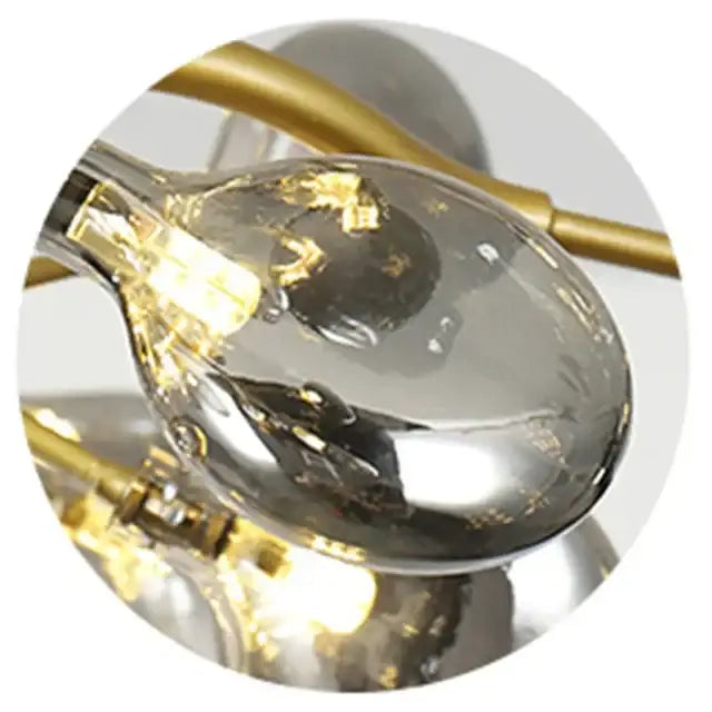 A clear teardrop glass pendant with gold-toned frame and filament bulb in decorbites branch iron black gold chandelier