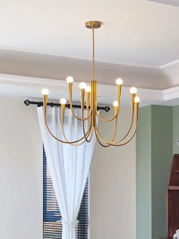 Gold-toned decorbites brass chandelier with multiple curved arms and glowing bulbs for dining room lighting