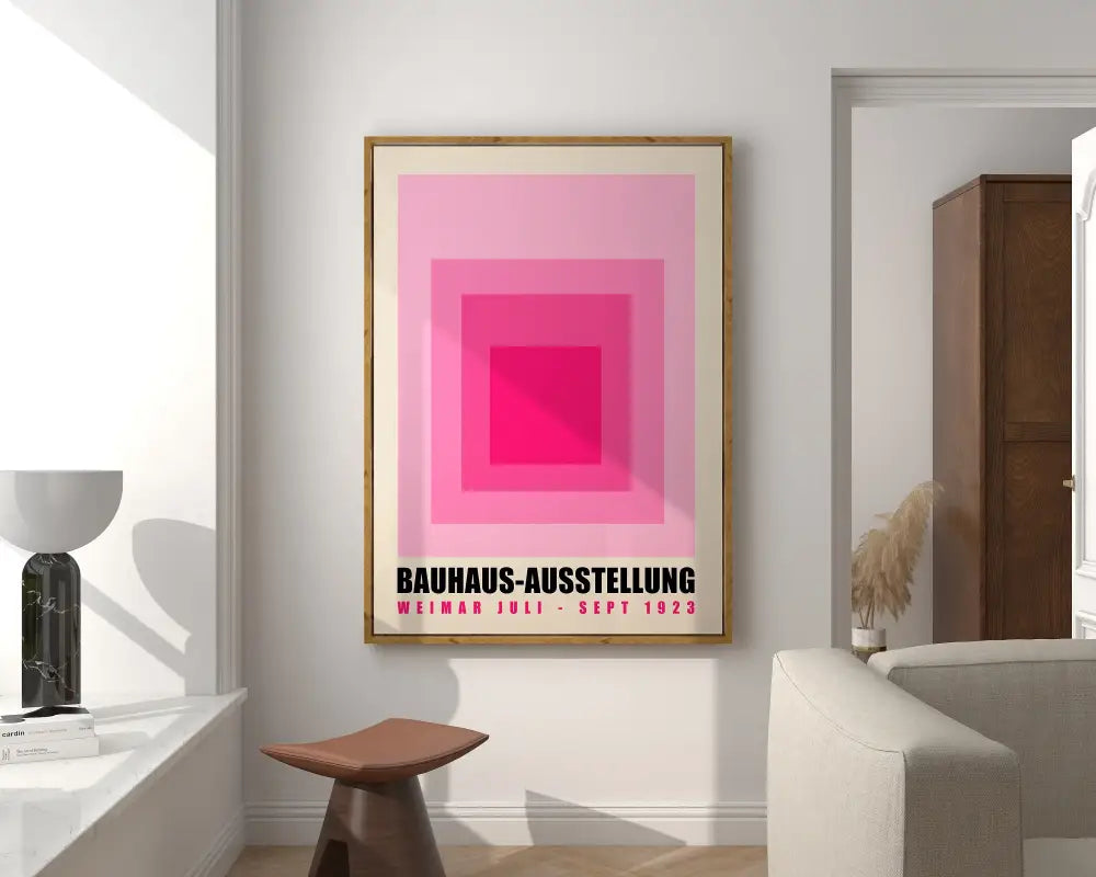 A bright geometric canvas print featuring bauhaus-style pink squares and black text in a light wood frame for home decor