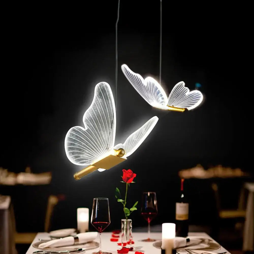 Two illuminated decorbites butterfly led pendant lights with translucent wings and gold bodies hang above dining table