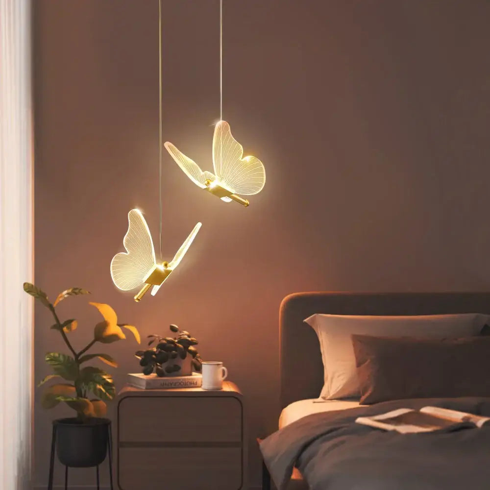 Two elegant decorbites butterfly led pendant lights with glowing translucent wings and gold bodies hang above a bedroom