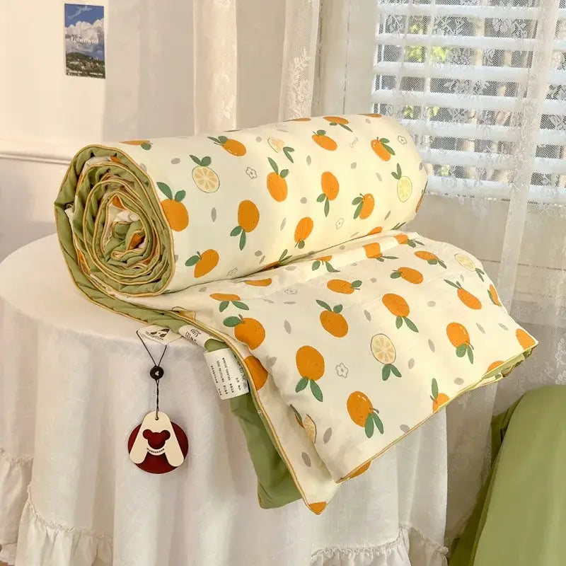 A cream-colored decorbites cartoon summer blanket with orange fruit pattern and olive green edges made of cotton