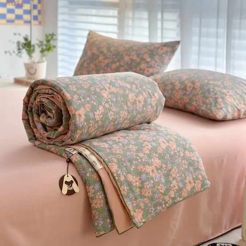A rolled-up decorbites cartoon summer cotton blanket with soft green and pink floral pattern and peach lining
