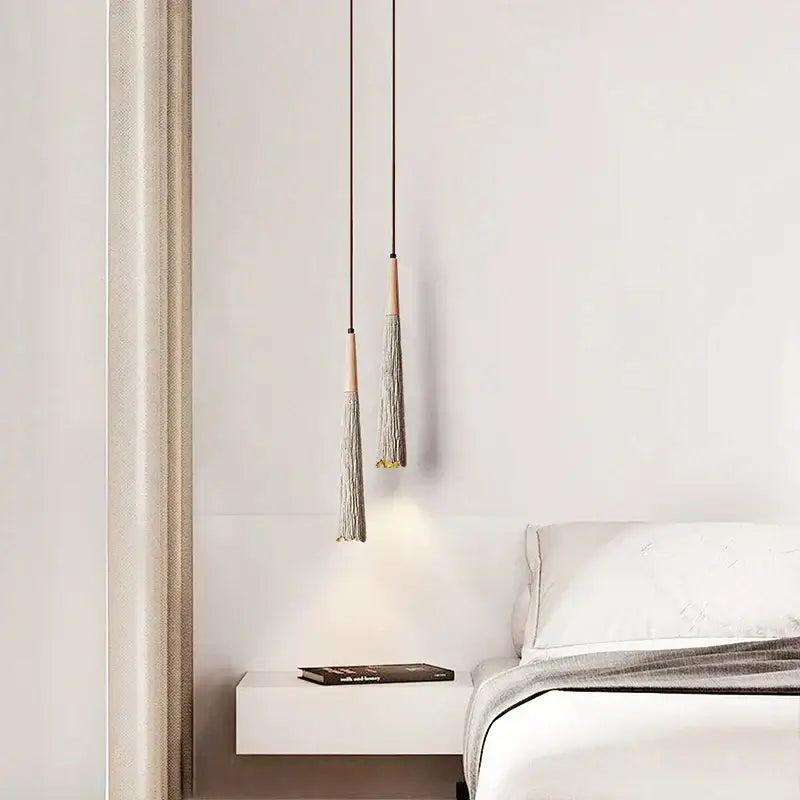 Two minimalist decorbites cement cream led pendant lights with wooden tops and gray tassels hang above a white bedside table