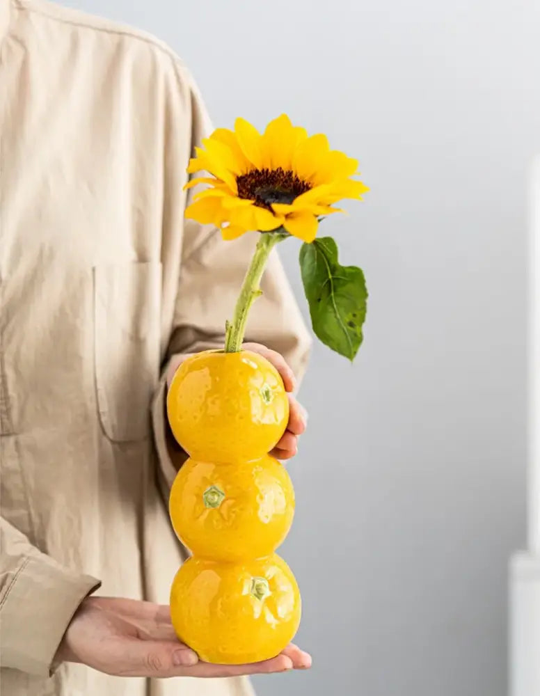 Bright yellow ceramic fruit vase shaped like stacked oranges holding a sunflower for home and office decor