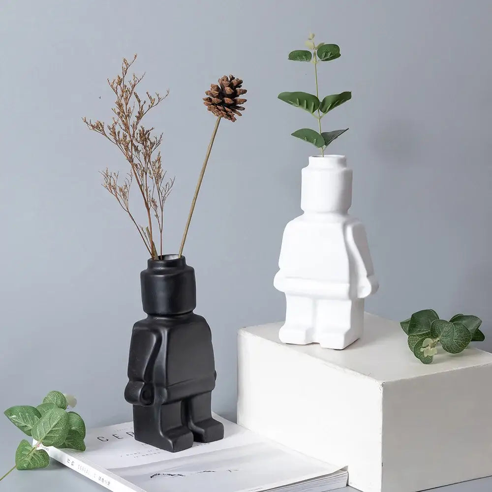 Black and white ceramic robot vases shaped like lego minifigures with dried plants in nordic style decor
