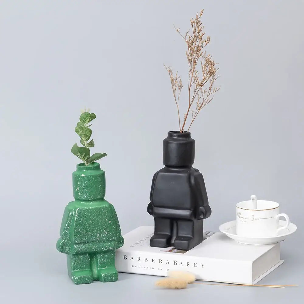 Green and black ceramic robot vases in nordic style shaped like lego minifigures holding greenery and dried flowers