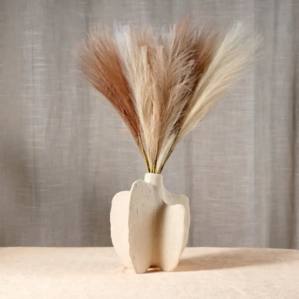 Cream-colored ceramic sea vase with organic nordic modern form holding dried beige and tan pampas grass bouquet