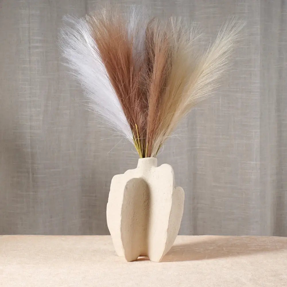 Cream-colored sculptural ceramic sea vase with modern abstract design holding white and beige pampas grass nordic modern decor