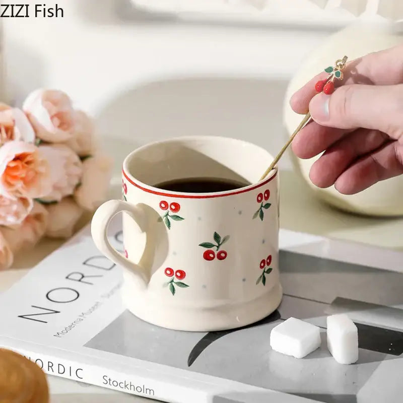 Cream-colored cherry pattern porcelain coffee mug with red cherry decals filled with dark liquid for afternoon tea