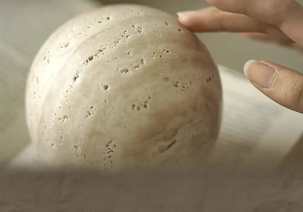 A smooth off-white chestnut stone sphere with natural porous texture featuring wabi sabi wind design decor ornament