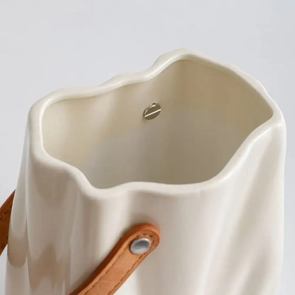 Cream-colored chic ceramic vase with a wavy rim and tan leather strap for elegant home decoration by DecorBites