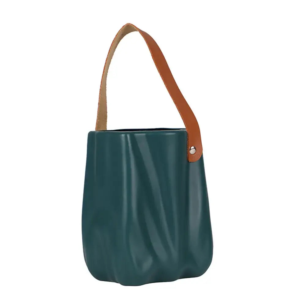 Teal-green textured bucket bag with tan leather handle and silver hardware beside decorbites™ chic ceramic vase for home decoration