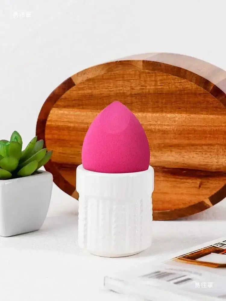A vibrant pink makeup sponge with soft texture resting in a white ceramic chicken shape egg cup holder by decorbites