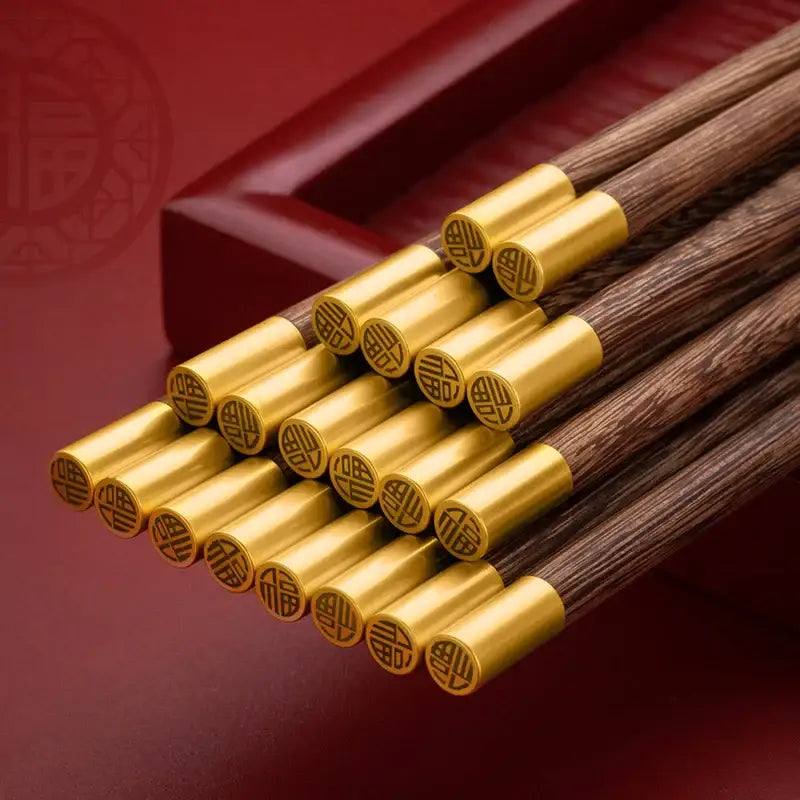Set of elegant dark wood chicken-wing wood chopsticks with polished gold metal tips engraved with traditional chinese characters