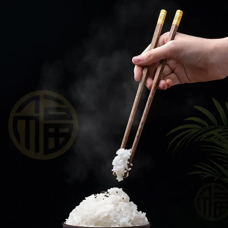 A pair of elegant gold-tipped wood chopsticks delicately holding steaming white rice from the decorbites wood chopsticks set