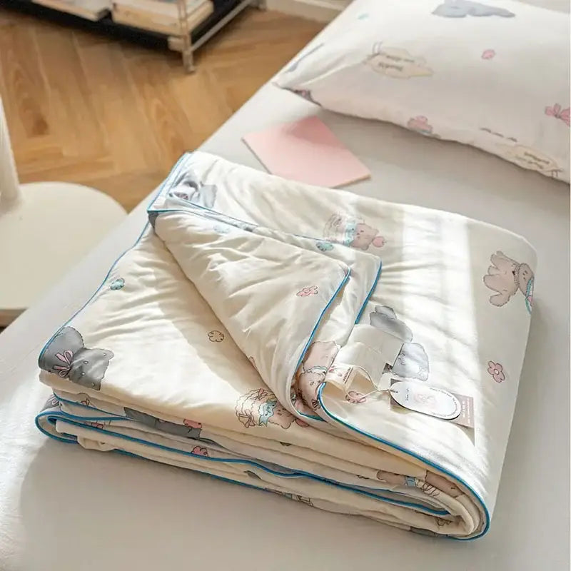 A cream-colored decorbites children cartoon cooling quilt with elephant and flower pattern and teal border for double bed