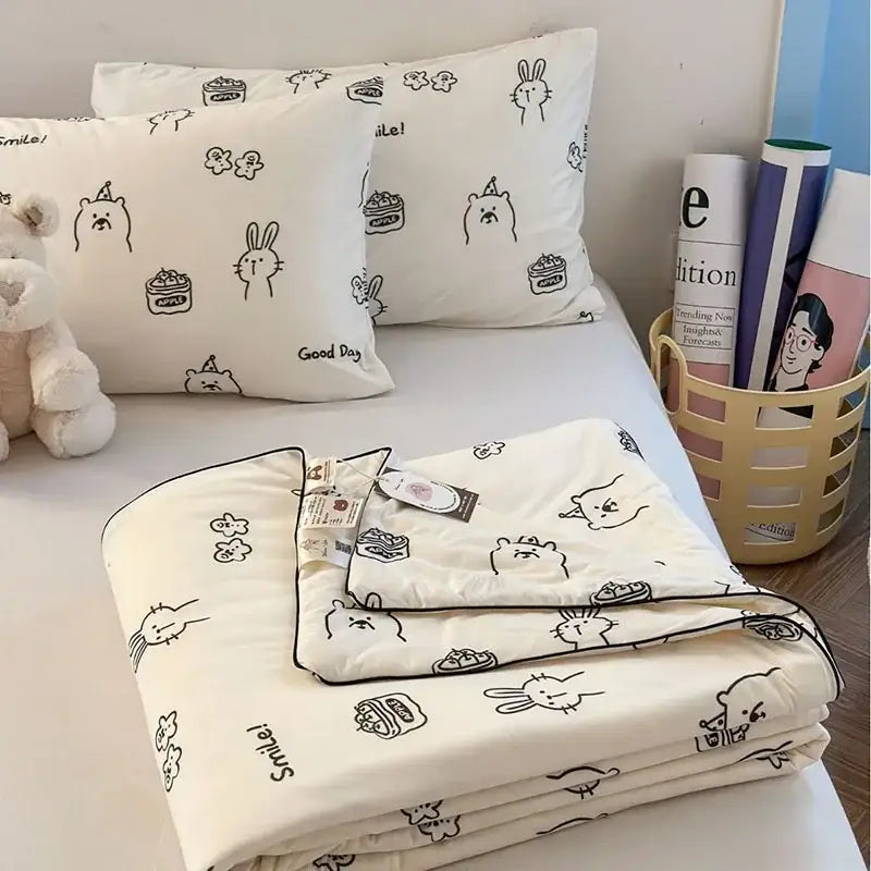 Cream-colored decorbites children cartoon summer cooling quilt with black animal and cake patterns neatly folded on bed