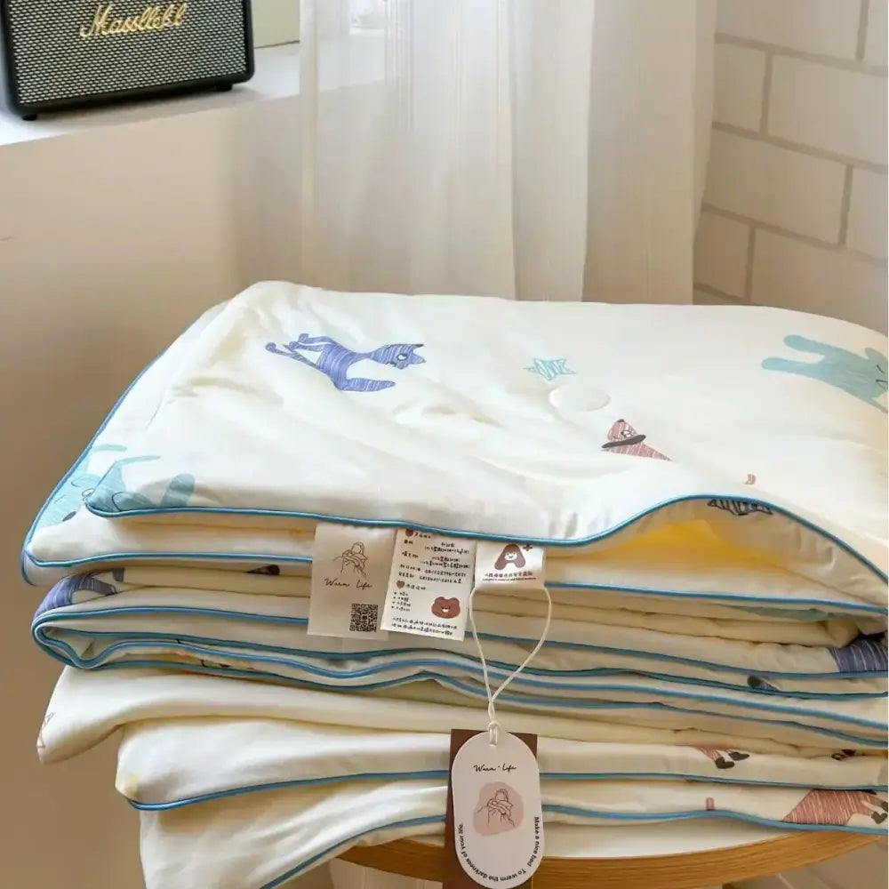 A cream-colored decorbites children cartoon summer cooling quilt with blue and pink animal prints in soft cotton