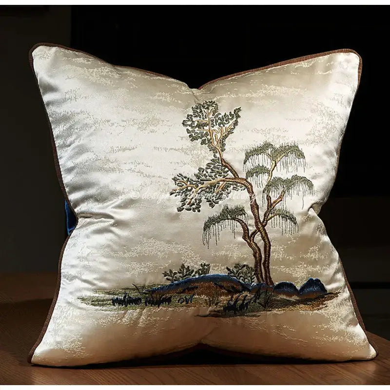 Cream-colored satin pillow cover with chinoiserie landscape embroidered featuring tree and mountains in green brown and blue