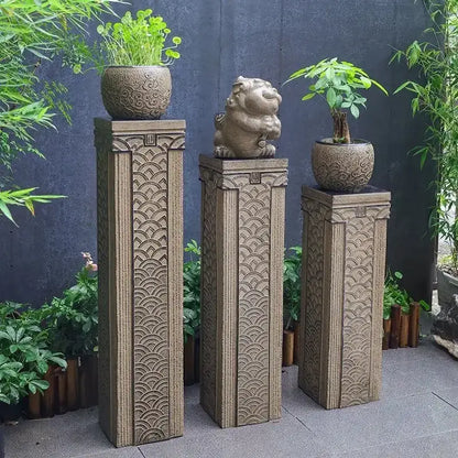 Three beige stone DecorBites stake display columns with intricate wave carvings topped with plants and lion statues