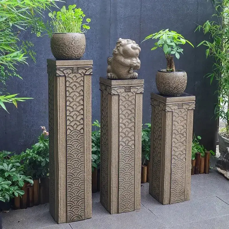 Three beige stone DecorBites stake display columns with intricate wave carvings topped with plants and lion statues