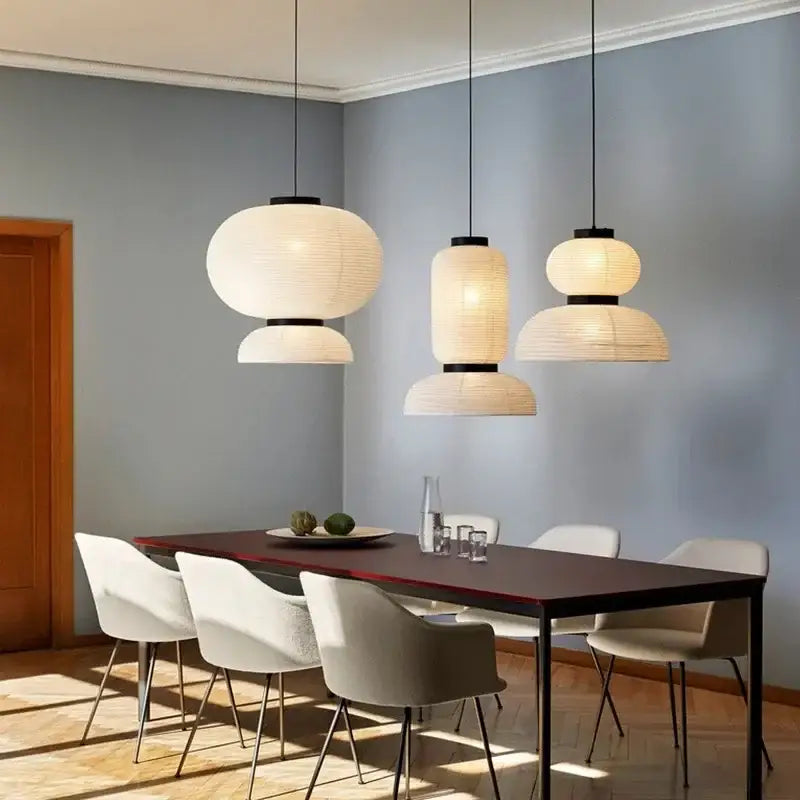 Three modern decorbites pendant lights with paper lantern shades and black metal fixtures hanging above a dining table